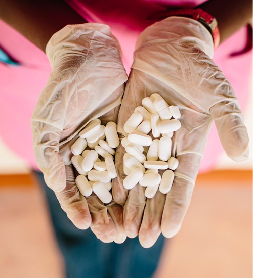 Two hands holding dozens of pills.